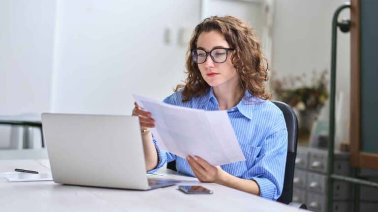 Frau liest DIN-A4-Papier vor Laptop: Rundum abgesichert – der Mayflower-360-Grad-Krankenversicherungs-Check