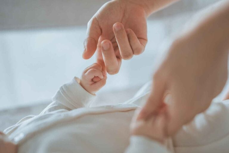 Mayflower "bärenstark" Konzept - Absicherung für Kinder. Eltern halten Hände von Baby.