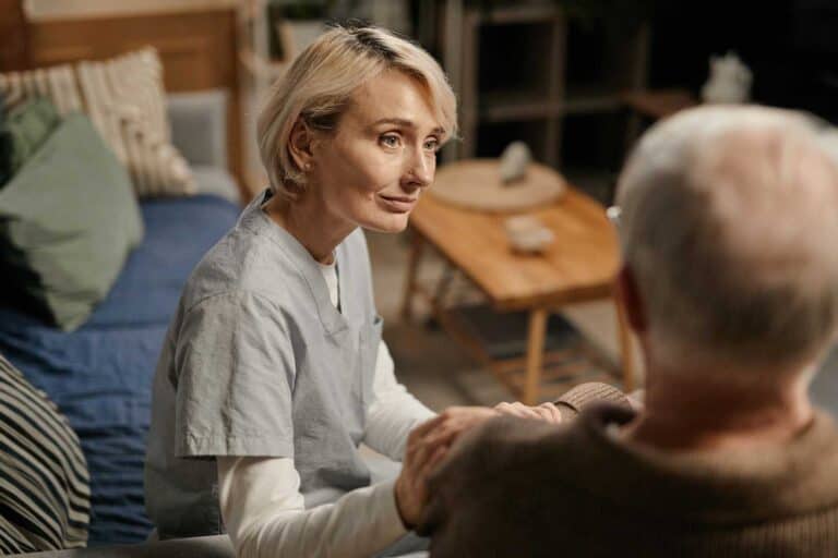 Eine Pflegerin sitzt neben einem Senior und hört ihm zu - abgesichert sein dank Pflegeversicherung